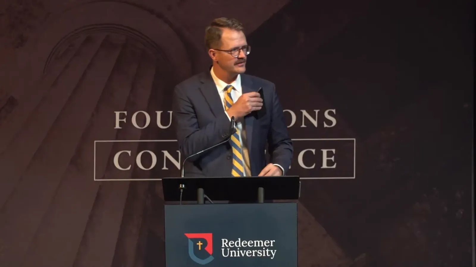 Colin Postma at the podium of the Foundations Conference, with his name title on screen: Interim Executive Director, ARPA Canada